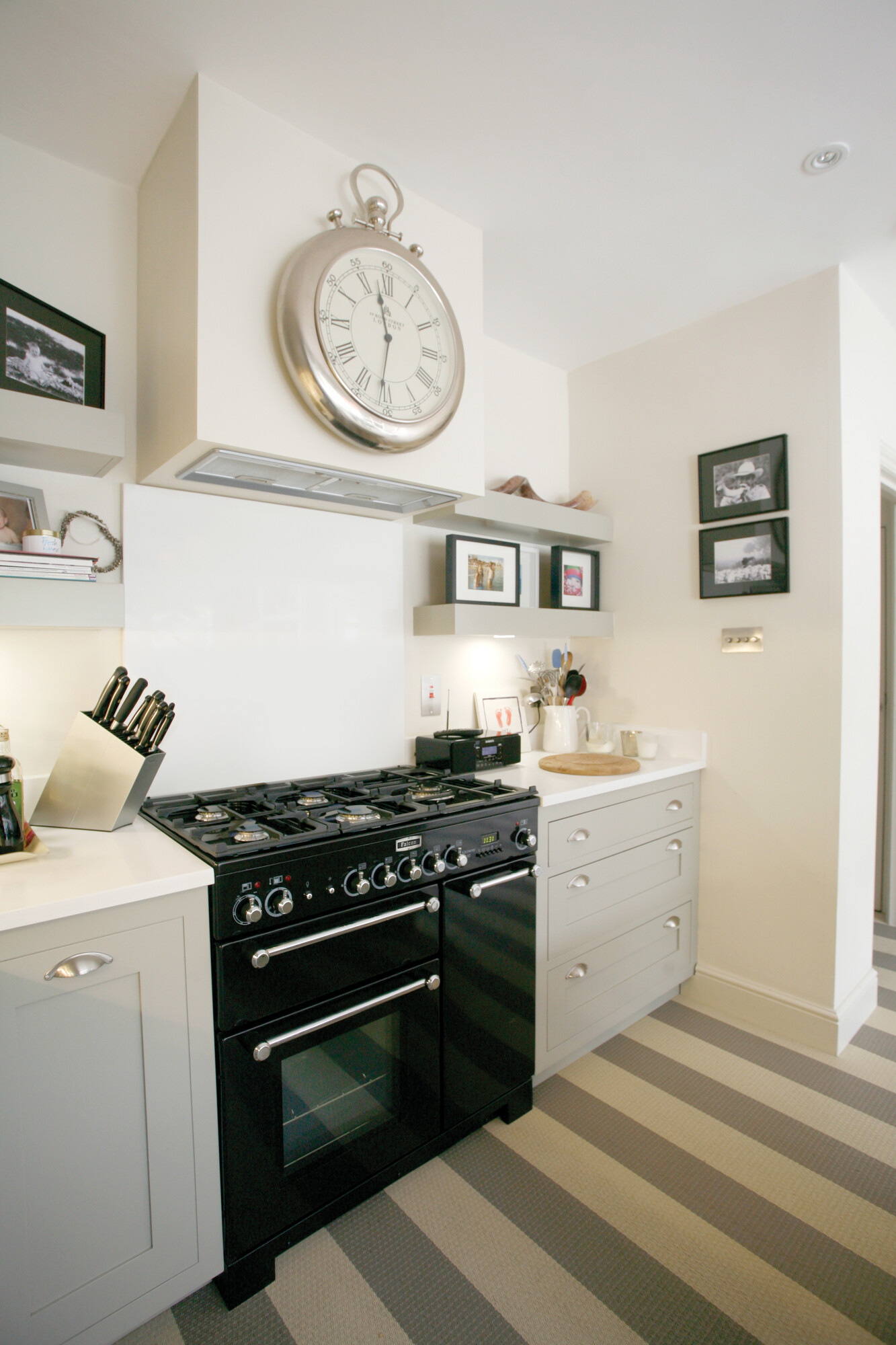 Helle Küche mit schwarz-silbernem Gasherd, silberner Wanduhr, Messerblock und modernen Hängeregalen mit Bildern