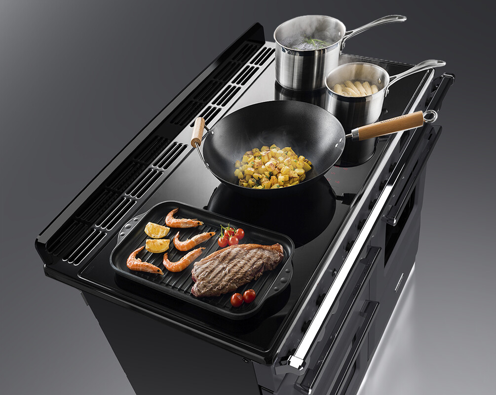 Induktionsherd mit Grillpfanne, Wok sowie zwei Kochtöpfen, auf denen Garnelen, Fleisch, Gemüse und Spargel gekocht werden