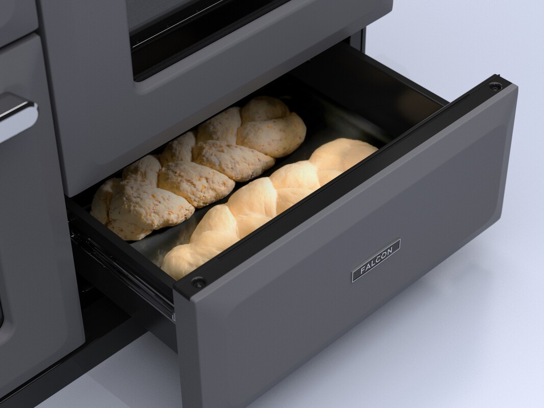 Backofenschublade einer Küche geöffnet, darin frische Brötchen und geflochtenes Gebäck auf Backblech, Marke Falcon sichtbar