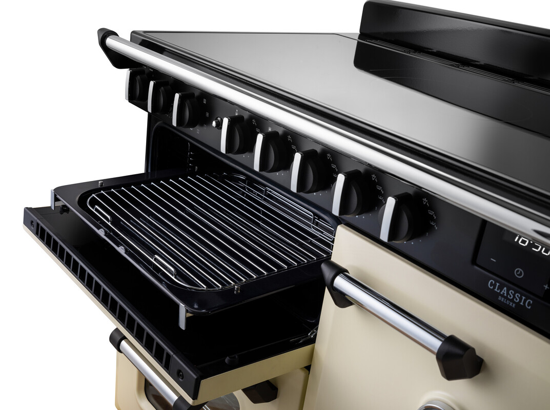 Detailaufnahme: moderner Standherd in Creme mit schwarzem Induktionskochfeld; geöffneter Grill/Backofen mit Auszug-Grillpfanne und Rost, ergonomische Drehknebel und stabiler Türgriff – ideal zum präzisen Kochen und Backen