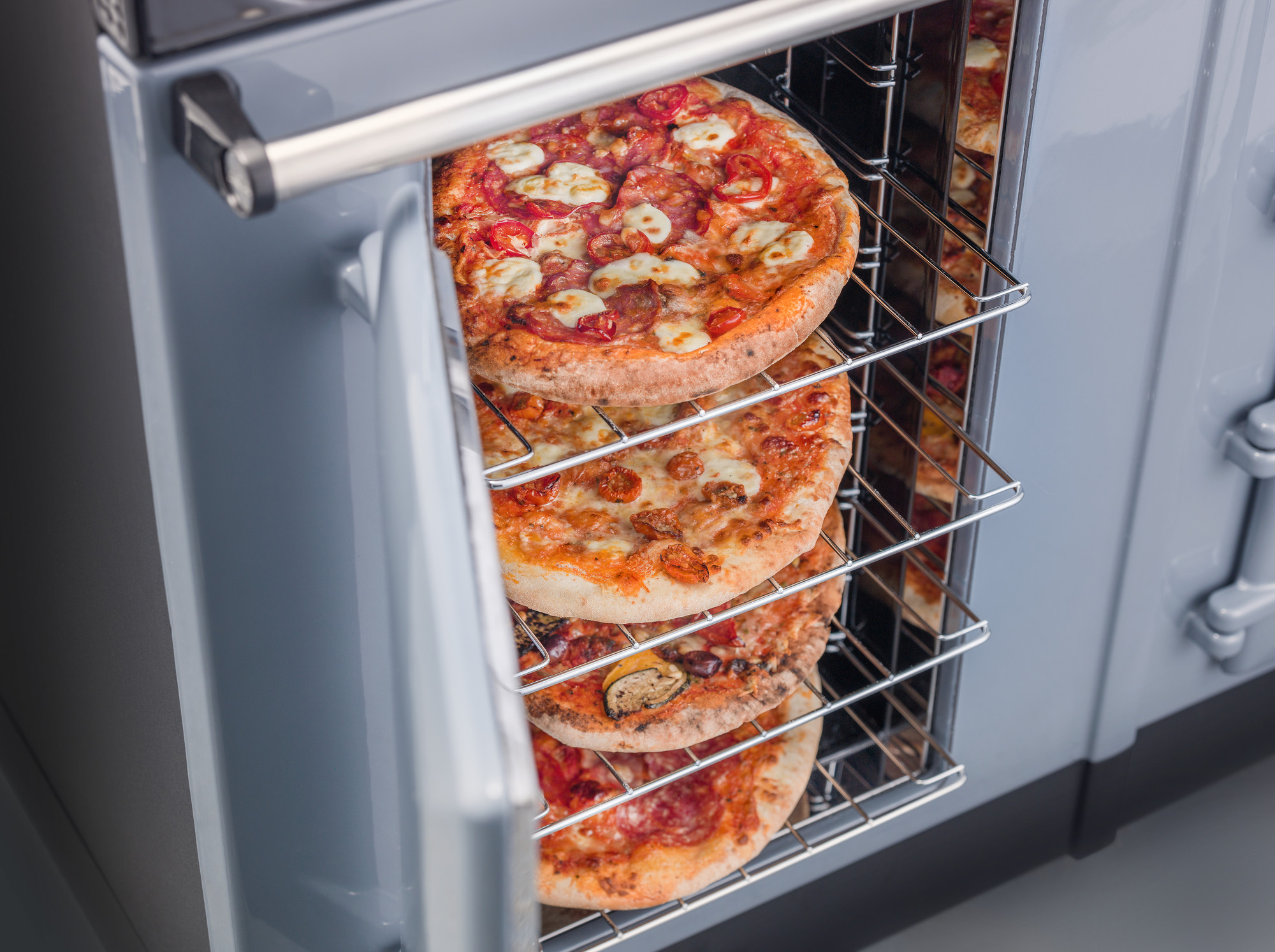 Mehrere belegte Pizzen werden gleichzeitig auf den Gitterrosten eines geöffneten Ofens gebacken