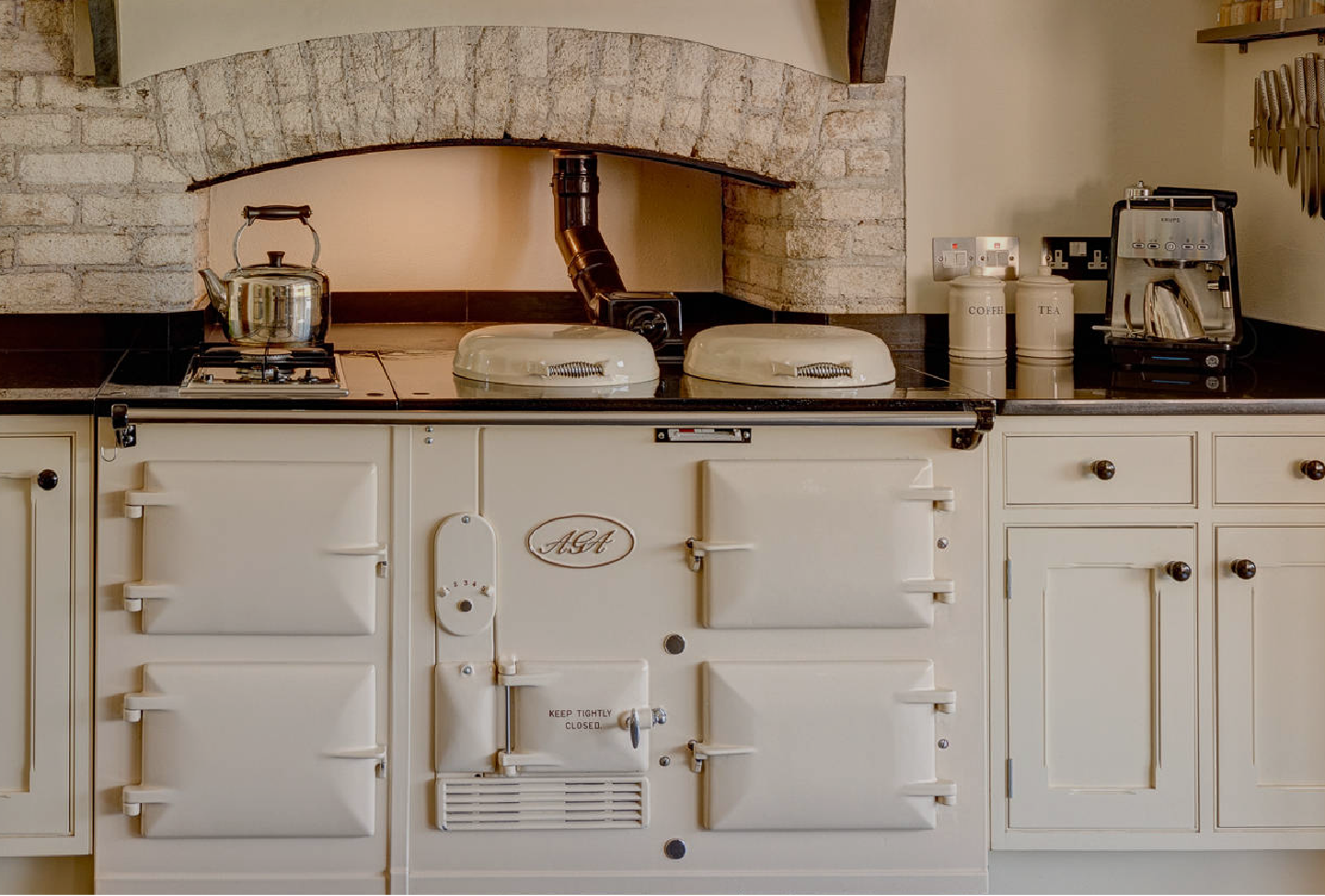 Traditioneller AGA-Herd in einer rustikalen Küche, mit Wasserkocher, Kaffeemaschine und Tee- und Kaffeebehältern auf der Arbeitsplatte