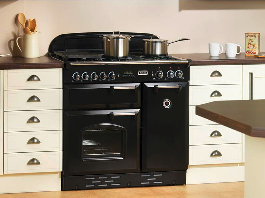 Schwarzer Standherd mit Gas-Kochfeld und zwei Edelstahltöpfen, eingebaut in eine helle Landhausküche mit weißen Schubladen