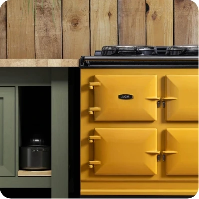 Gelber AGA-Herd neben grünen Schränken und Holzwandverkleidung