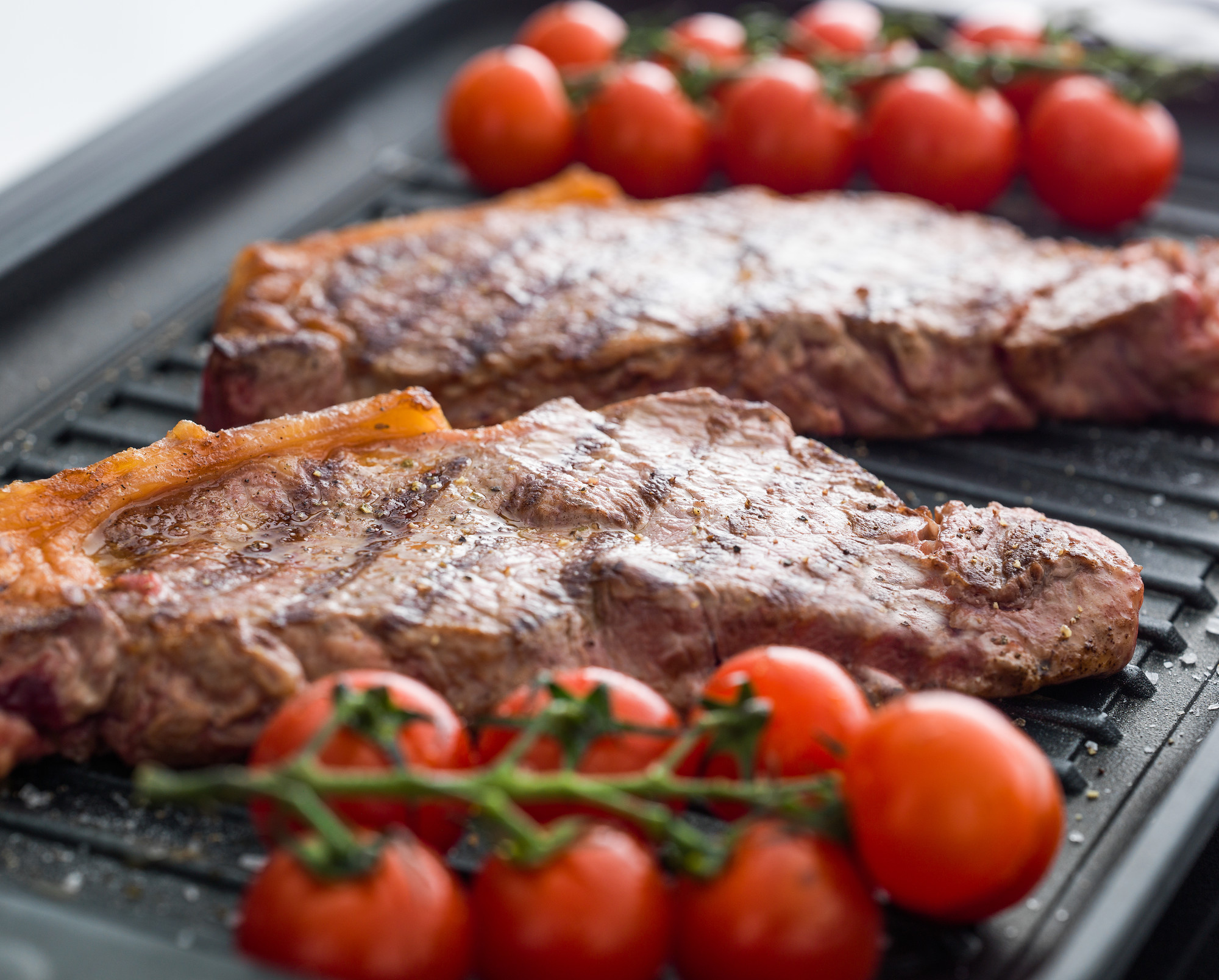 Zwei gegrillte Rindersteaks mit aromatischer Kruste und frischen Kirschtomaten auf einem Grillrost