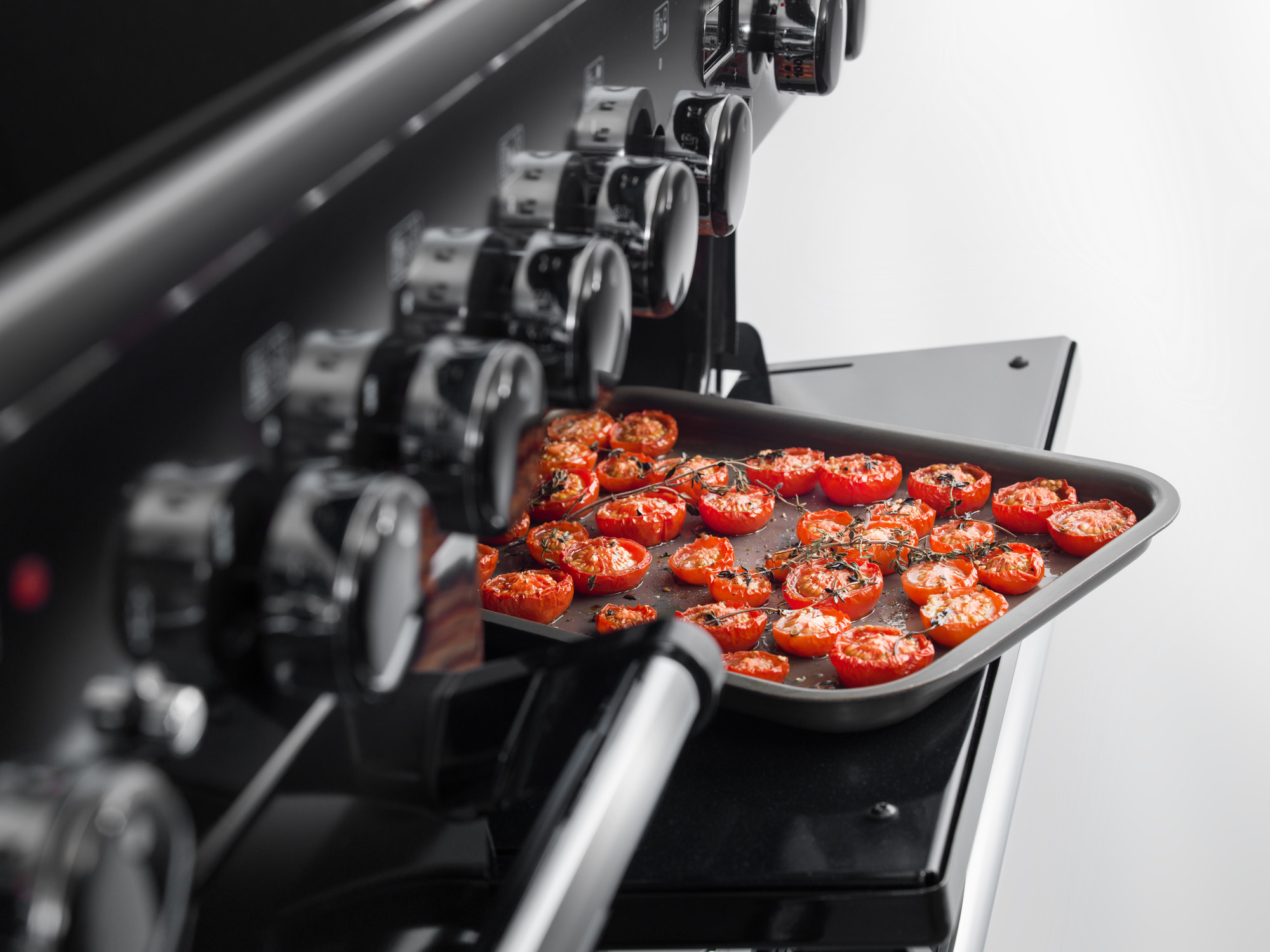 Nahaufnahme von halbierten, mit Kräutern gewürzten Tomaten auf einem Backblech in einem modernen Ofen