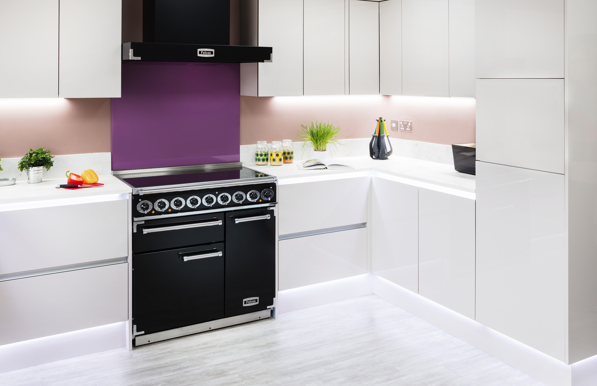 Helle, moderne Küche mit glänzenden, weißen Schränken, schwarzem Herd, lila Wandpaneel und Dekoration wie Kräutern und bunten Küchenutensilien