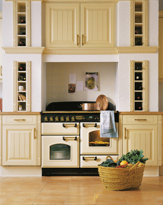 Elegante Landhausküche mit cremefarbenem Herd, Weinfächern, klassischen Schränken und einem Korb mit frischem Gemüse auf dem Boden