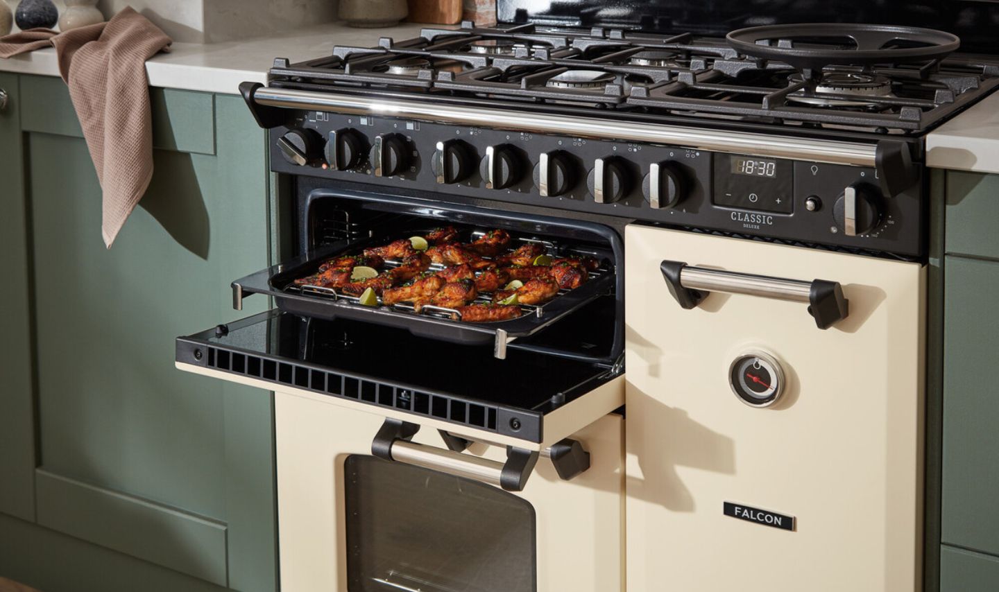 Cremefarbener Falcon Classic Deluxe Range Cooker mit Gas-Kochfeld, offenem Backofen und Backblech mit Hähnchenflügeln in moderner Küche