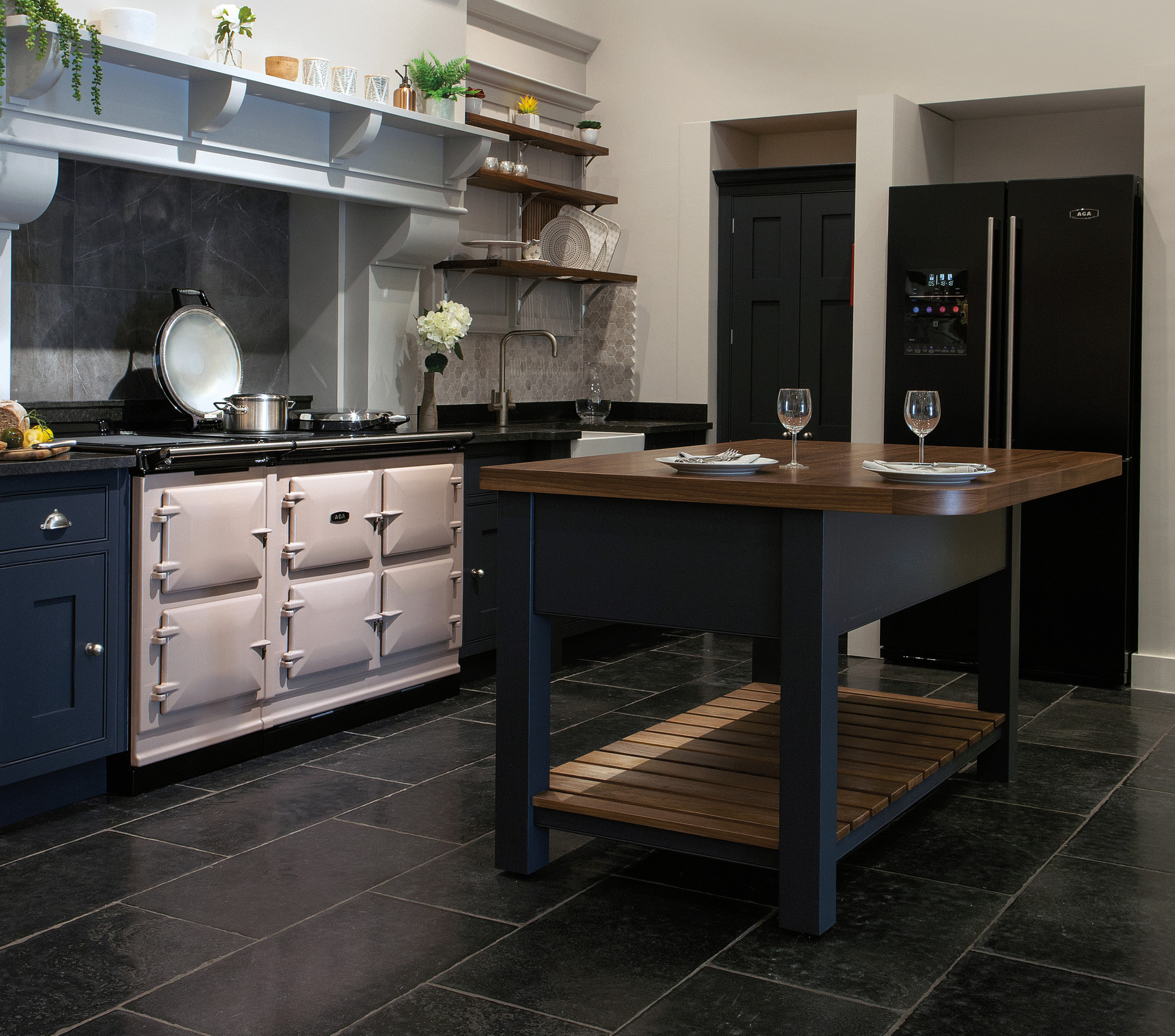 Küche im Landhausstil mit heller Kochinsel, offenem Regal, schwarzem Kühlschrank und gedecktem Tisch auf dunklem Fliesenboden