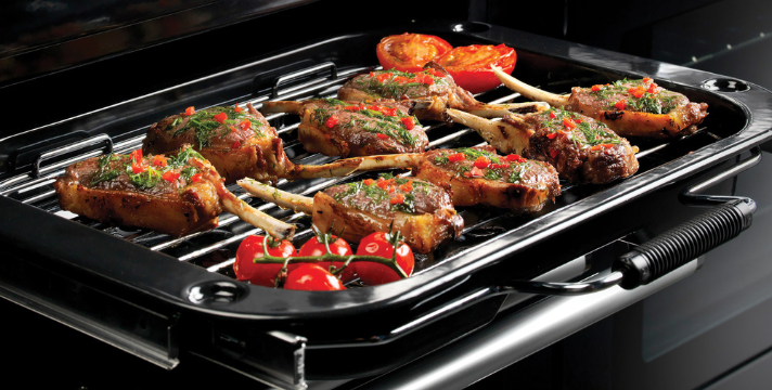 Mehrere gewürzte Lammkoteletts mit Kräutern und Tomaten werden auf einem Grill im Ofen gegart