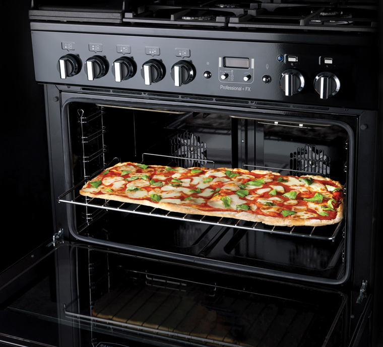 Offener Backofen mit einer großen rechteckigen Pizza mit Tomaten, Mozzarella und frischem Basilikum auf dem Rost