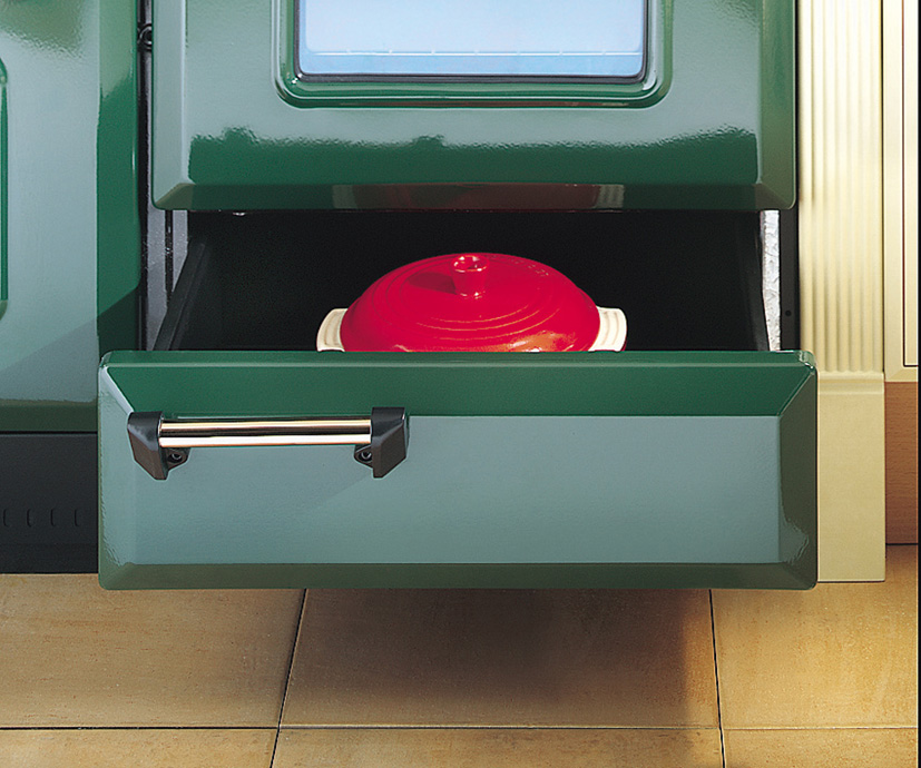 Detailaufnahme einer offenen, grünen Herdschublade, in der ein roter, runder Bräter aufbewahrt wird