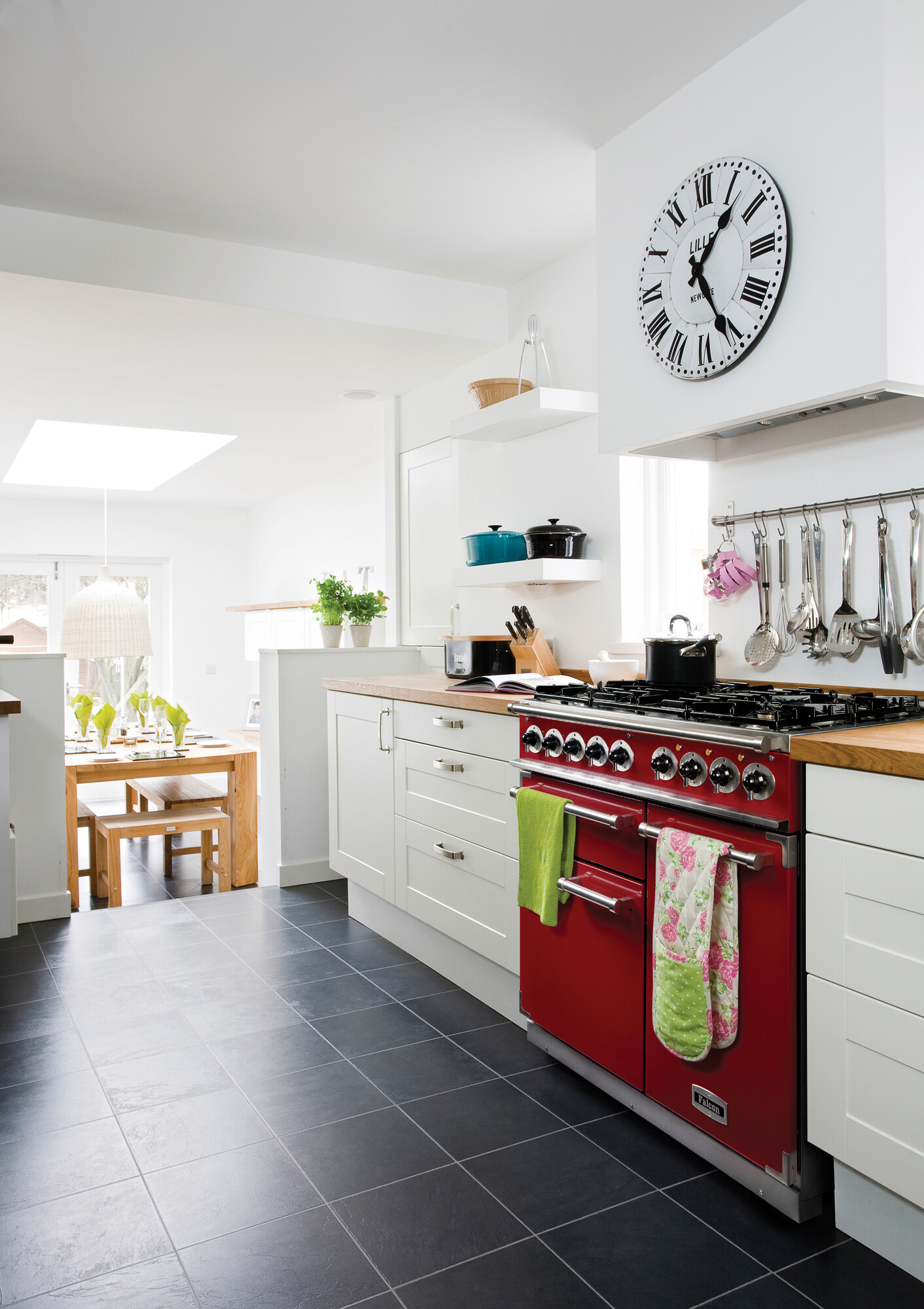 Elegante weiße Küche mit rotem Herd, großen Uhr an der Wand, und Sitzgruppe im Hintergrund, moderner Stil