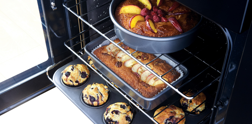 Drei verschiedene Backwaren im Ofen: Ein runder Obstkuchen, ein rechteckiger Apfelkuchen und mehrere Blaubeermuffins auf dem Blech