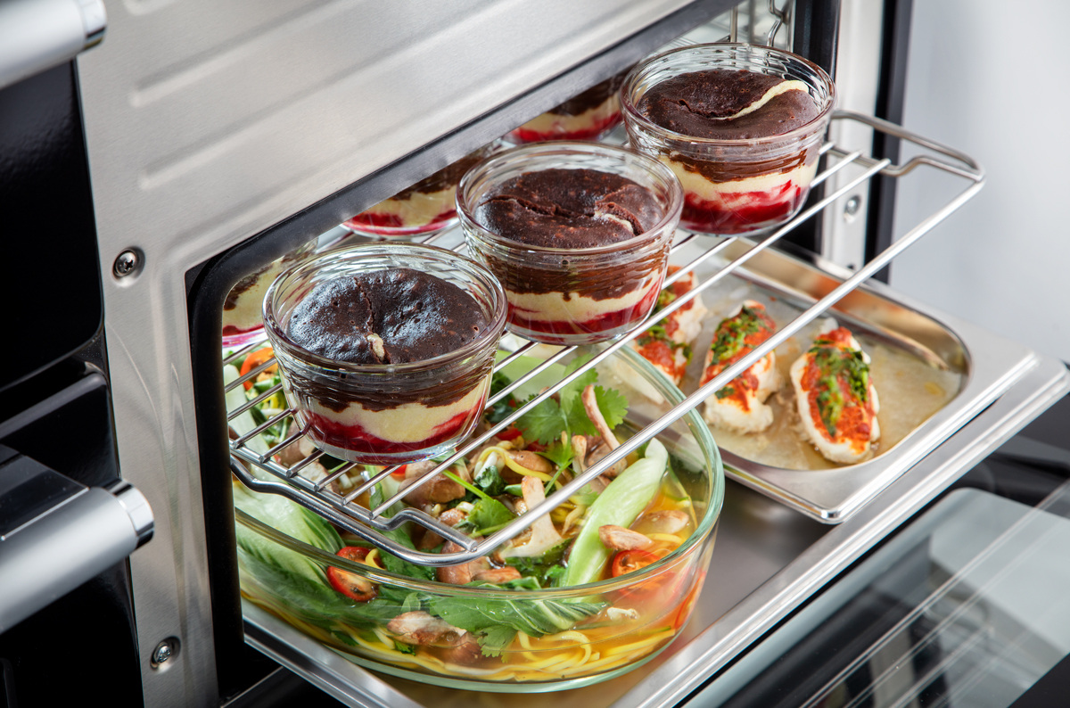 Ein geöffneter Ofen mit drei Schichtdesserts im Glas, gebackener gefüllter Hähnchenbrust und einer mit Suppe und Gemüse gefüllten Glasform