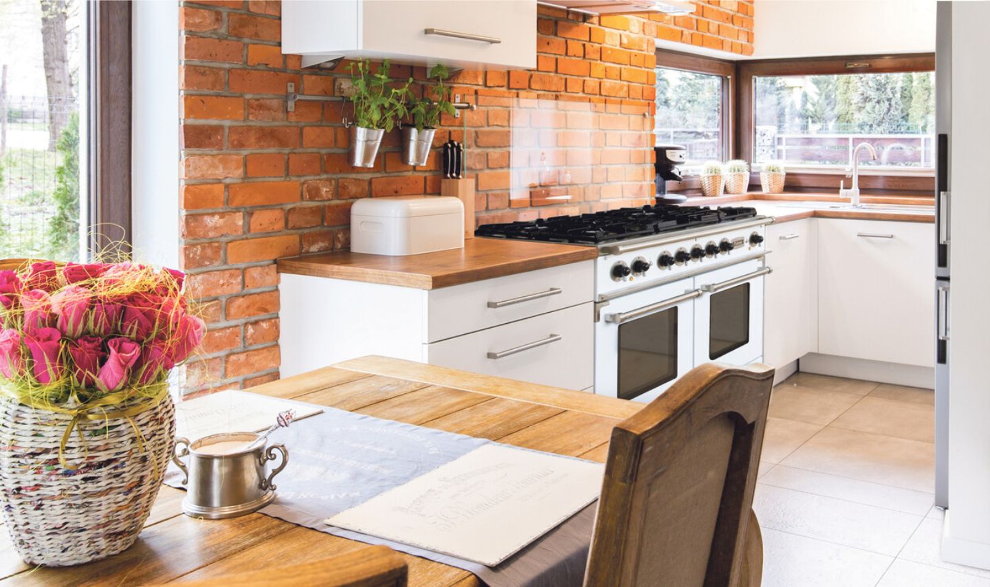 Helle Küche mit Ziegelwand, großem Gasherd und Spüle
