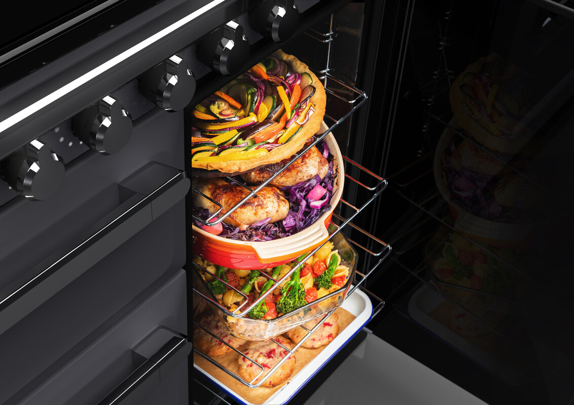Ofen mit mehreren Einschüben, auf denen Gemüse-Quiche, gebratene Hähnchenschenkel mit Rotkohl, Gemüseauflauf und Kekse gleichzeitig gebacken werden