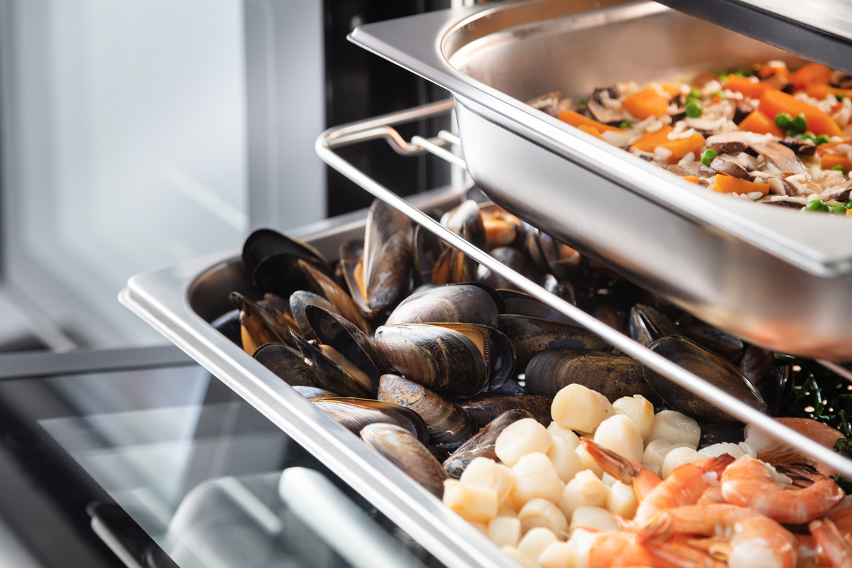 Nahaufnahme von frischen Muscheln, Garnelen und Jakobsmuscheln in einem Edelstahlbehälter, ideal für Buffets oder Gastronomie