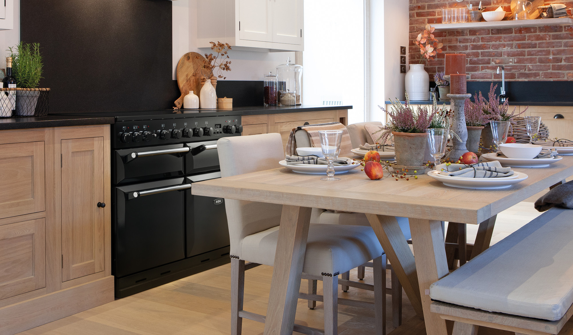 Helle Landhausküche mit Holzmöbeln, elegant gedecktem Holztisch, saisonaler Dekoration und einem schwarzen AGA Herd