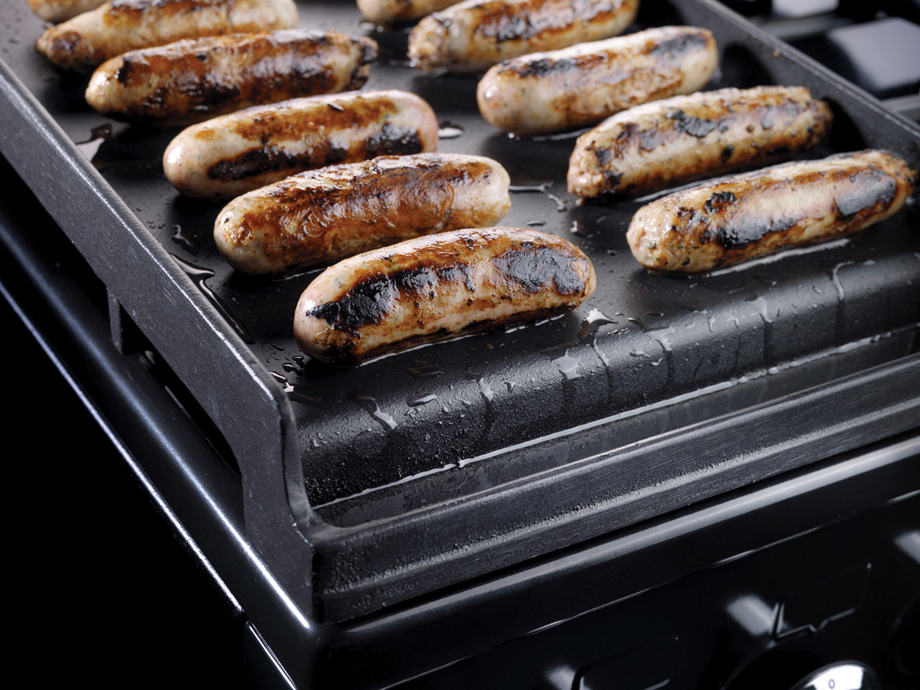 Mehrere gebräunte Bratwürste liegen auf einer heißen Grillplatte und werden gegrillt