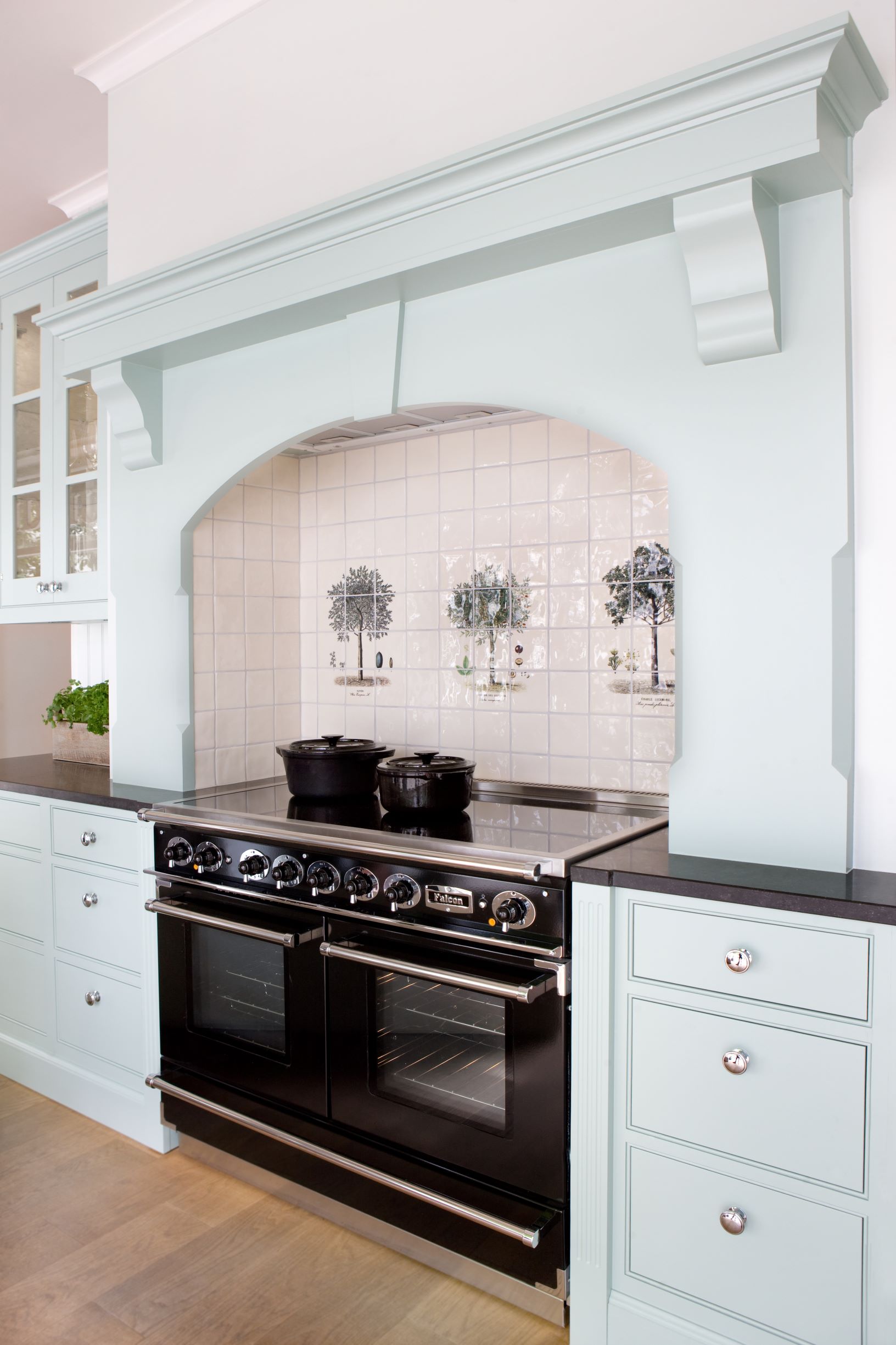 Moderner schwarzer Herd mit zwei Backöfen, umgeben von hellblauen Küchenschränken und dekorativem Fliesenspiegel mit Baum-Abbildungen