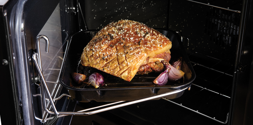 Frisch gewürzter Schweinebraten mit goldbrauner Kruste und roten Zwiebeln wird im Backofen auf einem Bratblech zubereitet