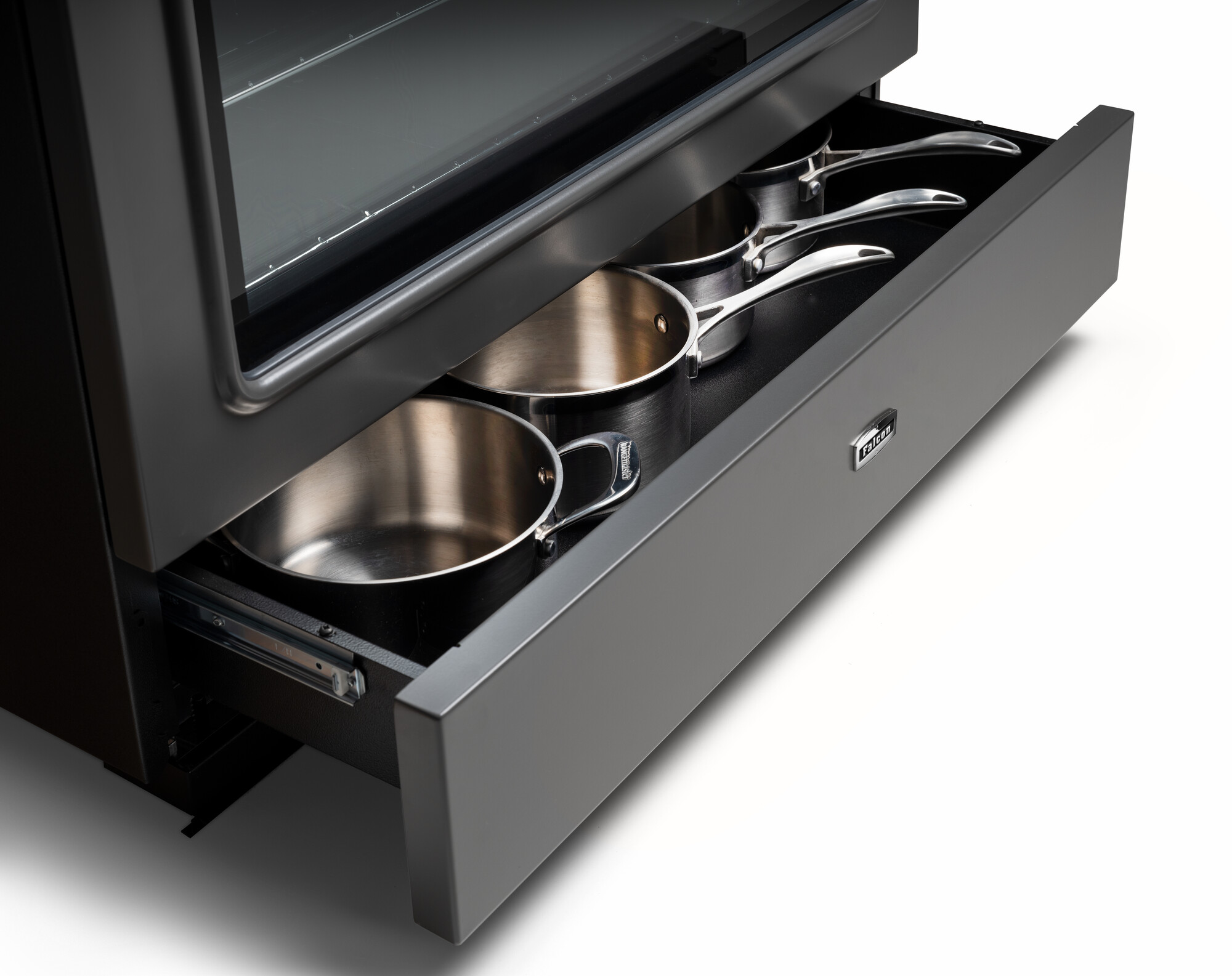 Geöffnete Schublade unter einem Backofen, in der drei Edelstahlpfannen ordentlich verstaut sind