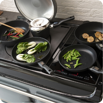 Induktionskochfeld mit mehreren Pfannen, die Gemüse wie Pak Choi, Zuckerschoten und Knoblauch zubereiten