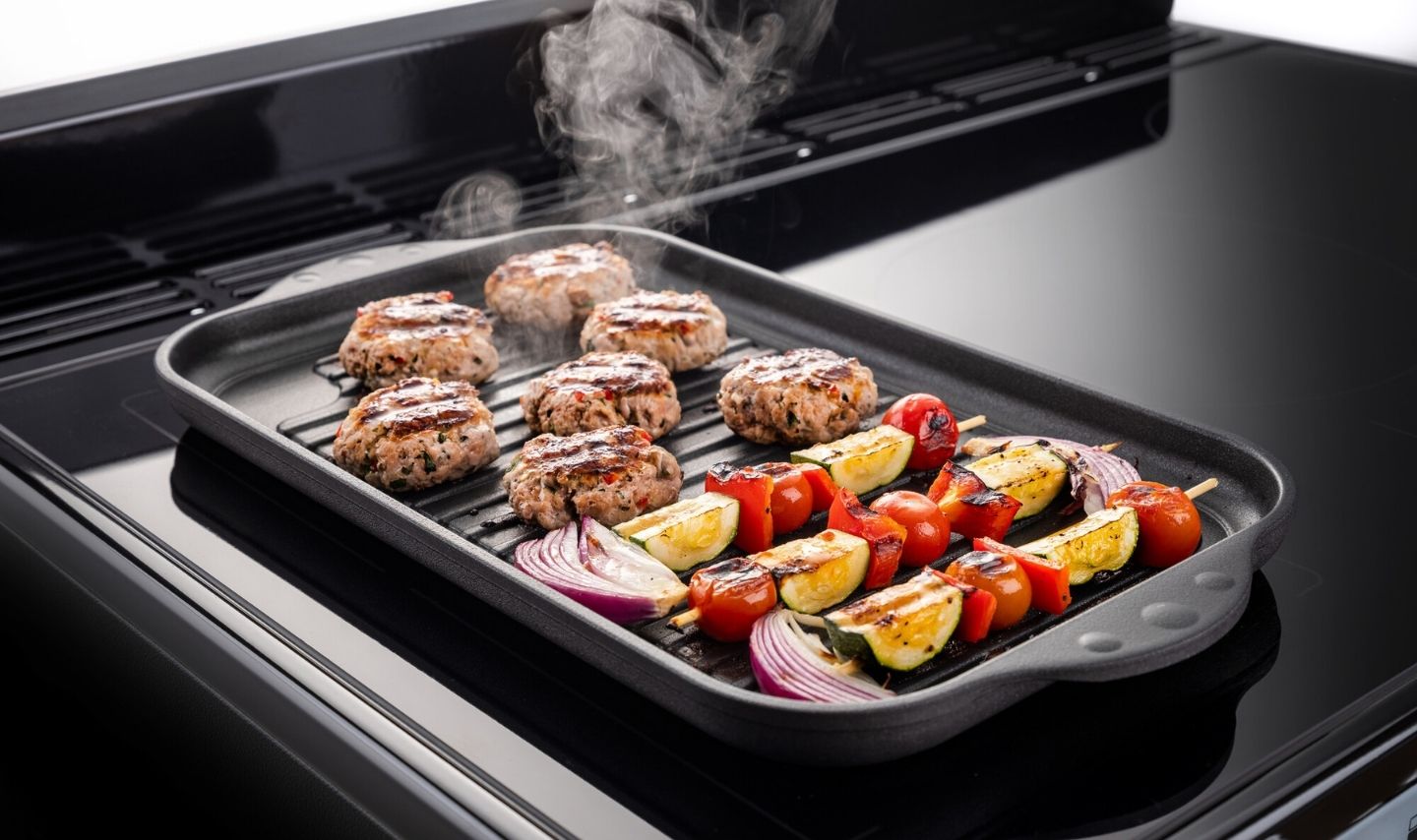 Rauchende Grillpfanne mit Patties und Gemüse auf dem Herd