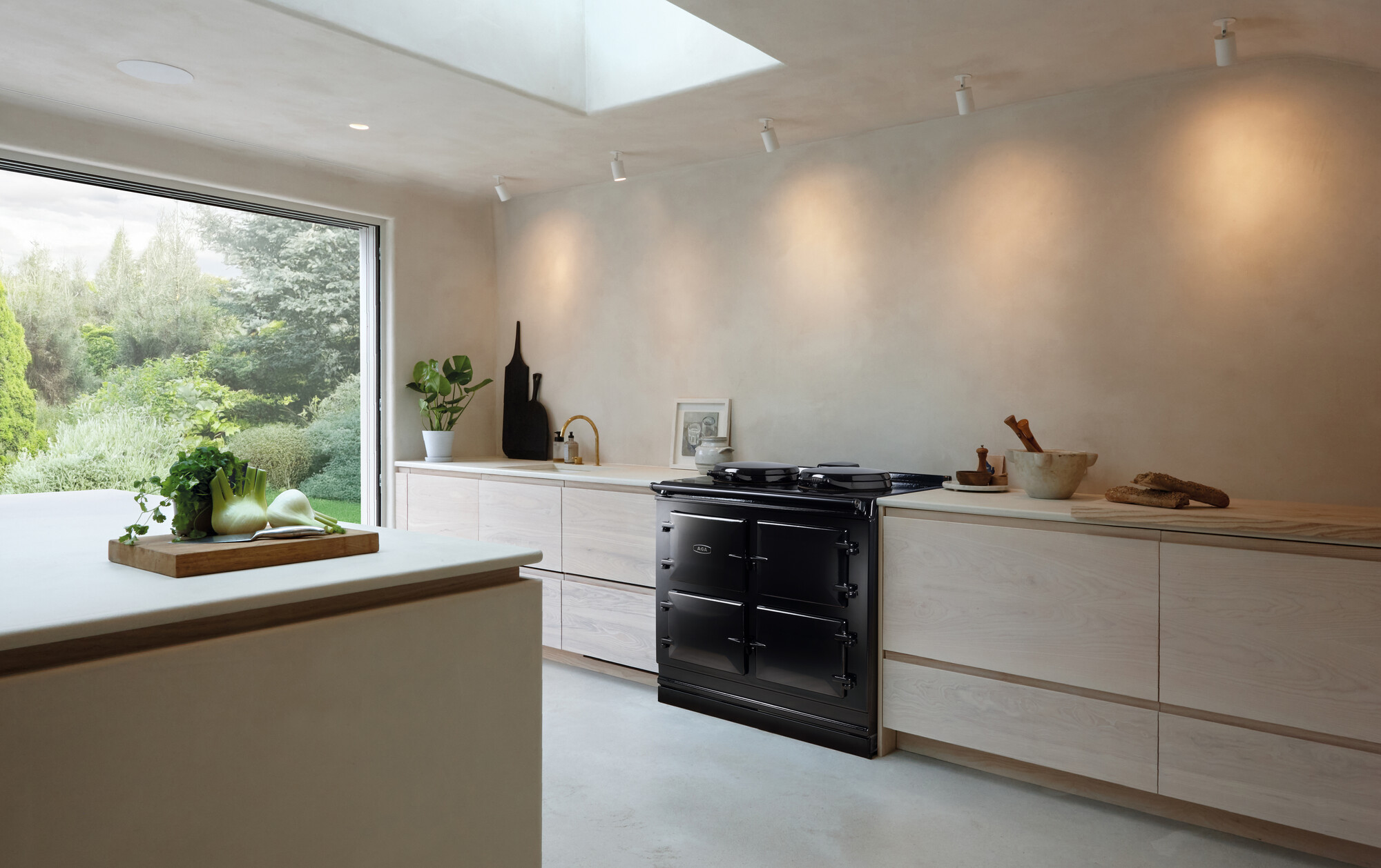 Geräumige, helle Designerküche mit schwarzem Herd, Holzmöbeln, Küchenutensilien und Blick in einen grünen Garten