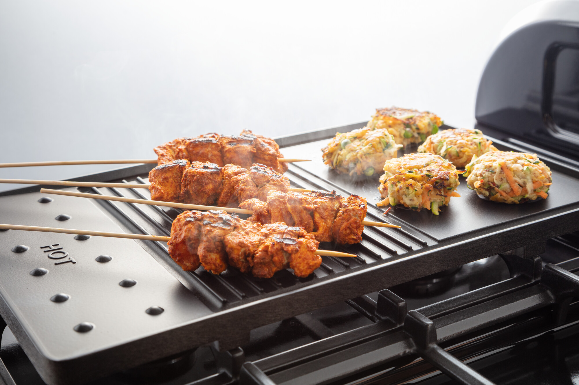 Fleischspieße und Gemüsepuffer werden auf einer gusseisernen Grillplatte auf einem Gasherd zubereitet