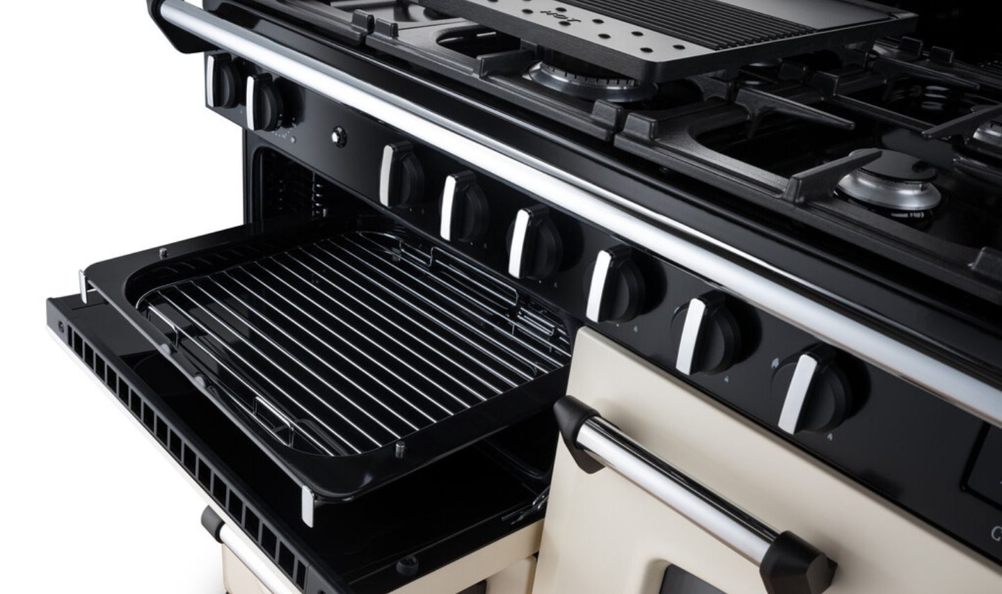 Detailansicht eines cremefarbenen Range-Standherds: Gaskochfeld mit mehreren Brennern, gusseiserne Topfträger, offener Backofen mit herausziehbarer Grillpfanne und Bedienelementen