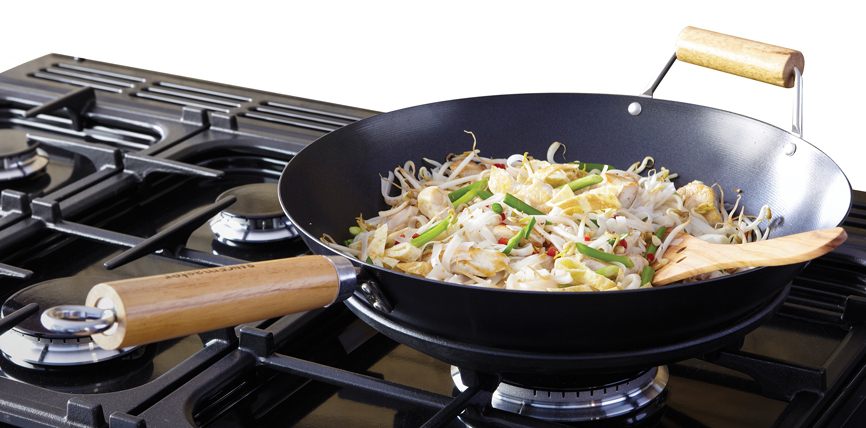 Schwarze Wokpfanne mit Holzgriffen, gefüllt mit Gemüse, Hähnchen und Sojasprossen, auf einem Gasherd