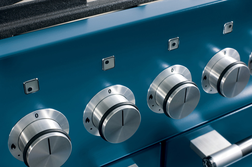 Nahaufnahme von vier Edelstahl-Drehknöpfen an einem blauen Gasherd, ideal für präzises Kochen